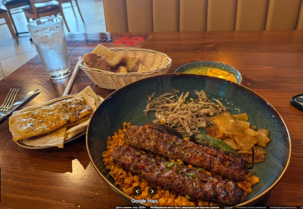 Adana kebab served over bulgur pilaf with grilled peppers and onion salad