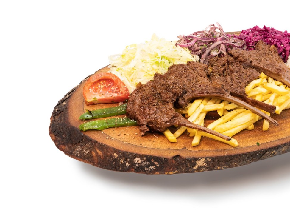 Grilled lamb chops served on a rustic wood board with fries, salad, and pickled cabbage